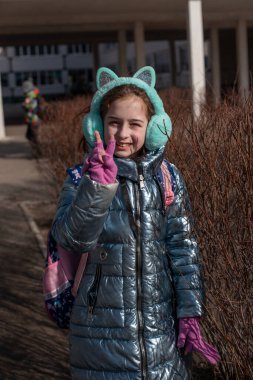 Mavi ceketli güzel genç bayan poz veriyor. Moda tarzı giysiler. Kışın açık havada mavi ceketli güzel bir kız. 9 yaşında. Okuldan çıkarılmış sırt çantalı bir kız. Kız seviniyor.