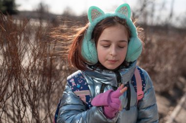 Mavi ceketli güzel genç bayan poz veriyor. Moda tarzı giysiler. Kışın açık havada mavi ceketli güzel bir kız. 9 yaşında. Okuldan çıkarılmış sırt çantalı bir kız. Kız seviniyor.