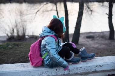 Güzel genç bir kadının portresi. Kışın nehir kenarında Plein hava çekimi. Bir gencin portresi. Kız 9 yaşında. Öğrenci kızlar sırt çantasıyla nehrin yanında yürürler. Kış, nehir