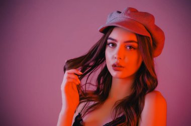 Göz kamaştırıcı genç kadın gri duvarda dalgalı saçlarıyla şık bir elbise giyiyor. Siyah elbiseli ve gri şapkalı bir kız elini öne uzattı. Kahverengi kıvırcık saçlı güzel bir genç kız. portre