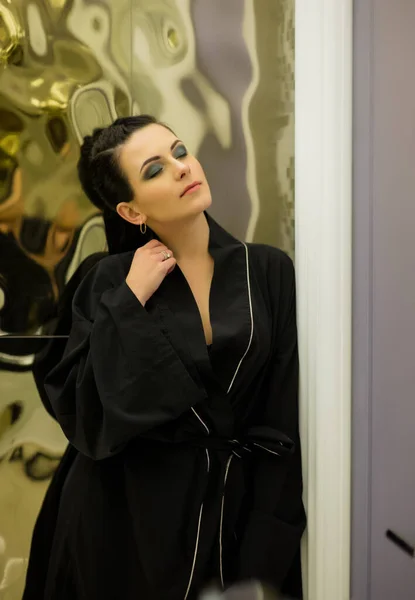 young woman posing in black silk bathrobe. sexy housewife concept. Girl in a black bathrobe indoors. Portrait of a girl. Brunette. Girl with professional make-up. Beauty saloon. Smokey Ice Eye Makeup