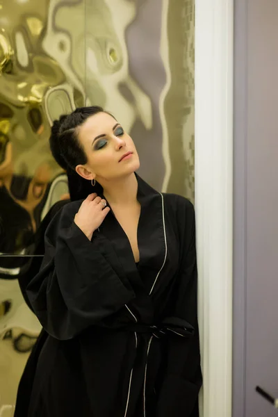 young woman posing in black silk bathrobe. sexy housewife concept. Girl in a black bathrobe indoors. Portrait of a girl. Brunette. Girl with professional make-up. Beauty saloon. Smokey Ice Eye Makeup