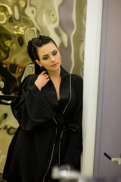 young woman posing in black silk bathrobe. sexy housewife concept. Girl in a black bathrobe indoors. Portrait of a girl. Brunette. Girl with professional make-up. Beauty saloon. Smokey Ice Eye Makeup