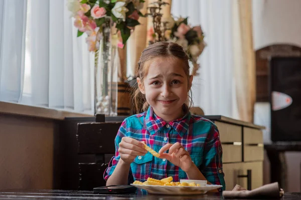 girl eating french-fries. Girl eating french fries in a cafe. A girl of 9 years old has lunch with french fries. French fries, sauce, lunch, food. A schoolgirl is eating and looking at a smartphone.