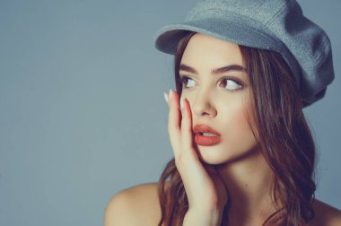 Göz kamaştırıcı genç kadın gri duvarda dalgalı saçlarıyla şık bir elbise giyiyor. Siyah elbiseli ve gri şapkalı bir kız elini öne uzattı. Kahverengi kıvırcık saçlı güzel bir genç kız. portre