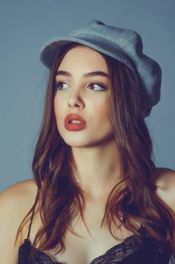 Göz kamaştırıcı genç kadın gri duvarda dalgalı saçlarıyla şık bir elbise giyiyor. Siyah elbiseli ve gri şapkalı bir kız elini öne uzattı. Kahverengi kıvırcık saçlı güzel bir genç kız. portre