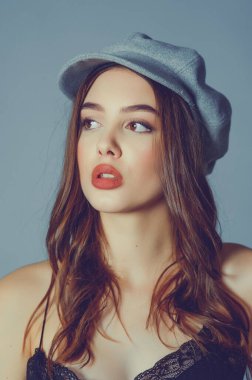 Göz kamaştırıcı genç kadın gri duvarda dalgalı saçlarıyla şık bir elbise giyiyor. Siyah elbiseli ve gri şapkalı bir kız elini öne uzattı. Kahverengi kıvırcık saçlı güzel bir genç kız. portre