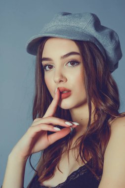 Göz kamaştırıcı genç kadın gri duvarda dalgalı saçlarıyla şık bir elbise giyiyor. Siyah elbiseli ve gri şapkalı bir kız elini öne uzattı. Kahverengi kıvırcık saçlı güzel bir genç kız. portre