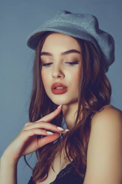 Göz kamaştırıcı genç kadın gri duvarda dalgalı saçlarıyla şık bir elbise giyiyor. Siyah elbiseli ve gri şapkalı bir kız elini öne uzattı. Kahverengi kıvırcık saçlı güzel bir genç kız. portre