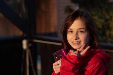 Dokuz yaşında güzel bir kızın portresi. Mutlu, gülümseyen, kendine güvenen 9 yaşındaki bir kızın portresi. Ahşap arka planda kırmızı kazaklı bir genç. Kızıl saçlı kız..