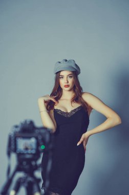 Göz kamaştırıcı genç kadın gri duvarda dalgalı saçlı şık bir elbise giyiyor. Siyah elbiseli ve gri şapkalı bir kız elini öne atıyor. Bir kız kamerada fotoğraflanıyor ya da ben video çekiyorum.