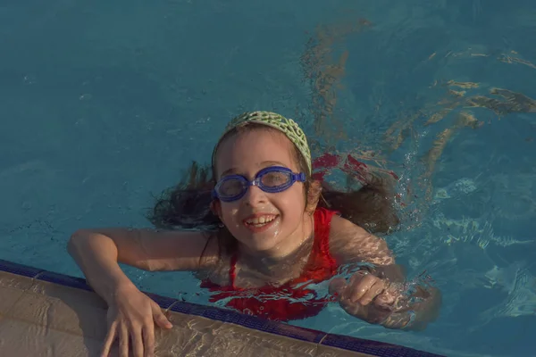 Cute girl with goggles in swimming pool. Girl swims in the pool with goggles. Summer, pool, relaxation, water park, relaxation area. The baby is swimming. Hello summer. Hooray, holidays. health