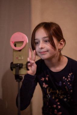 Mutlu genç bir kadın beyaz arka planda selfie çekiyor. Kız monopod ya da selfie çubuğuyla kendi videosunu çekiyor. Blogcu. Vlog. Kız internet ya da internet ağları için video çekiyor. Portre