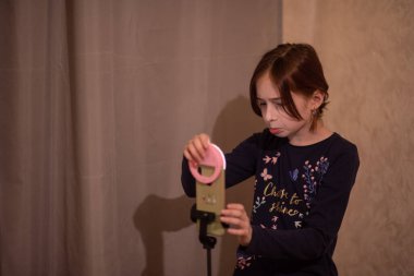 Mutlu genç bir kadın beyaz arka planda selfie çekiyor. Kız monopod ya da selfie çubuğuyla kendi videosunu çekiyor. Blogcu. Vlog. Kız internet ya da internet ağları için video çekiyor. Portre