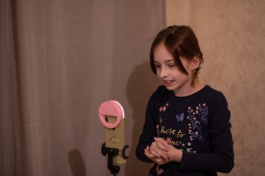 Mutlu genç bir kadın beyaz arka planda selfie çekiyor. Kız monopod ya da selfie çubuğuyla kendi videosunu çekiyor. Blogcu. Vlog. Kız internet ya da internet ağları için video çekiyor. Portre