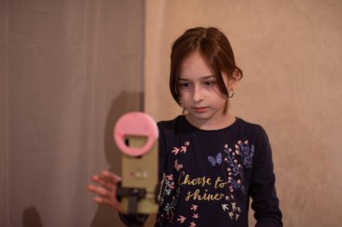Mutlu genç bir kadın beyaz arka planda selfie çekiyor. Kız monopod ya da selfie çubuğuyla kendi videosunu çekiyor. Blogcu. Vlog. Kız internet ya da internet ağları için video çekiyor. Portre
