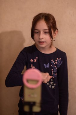 Mutlu genç bir kadın beyaz arka planda selfie çekiyor. Kız monopod ya da selfie çubuğuyla kendi videosunu çekiyor. Blogcu. Vlog. Kız internet ya da internet ağları için video çekiyor. Portre