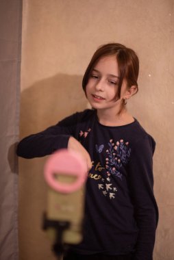 Mutlu genç bir kadın beyaz arka planda selfie çekiyor. Kız monopod ya da selfie çubuğuyla kendi videosunu çekiyor. Blogcu. Vlog. Kız internet ya da internet ağları için video çekiyor. Portre