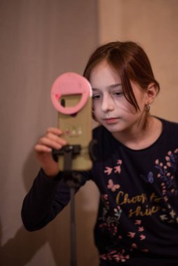 Mutlu genç bir kadın beyaz arka planda selfie çekiyor. Kız monopod ya da selfie çubuğuyla kendi videosunu çekiyor. Blogcu. Vlog. Kız internet ya da internet ağları için video çekiyor. Portre