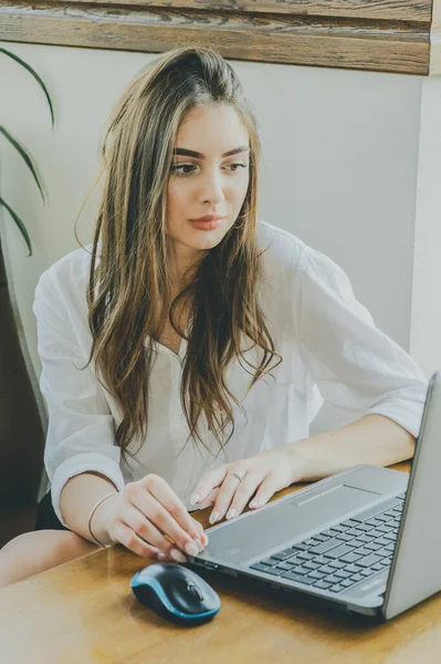 Young lady browsing the Internet at the cafe. Girl in a cafe with a laptop.Brunette girl with a gadget in the office. A woman is looking into a computer. Girl in a white shirt. Girl 18 or 19 years old