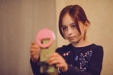 Mutlu genç bir kadın beyaz arka planda selfie çekiyor. Kız monopod ya da selfie çubuğuyla kendi videosunu çekiyor. Blogcu. Vlog. Kız internet ya da internet ağları için video çekiyor. Portre