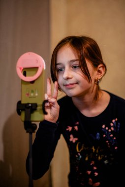 Mutlu genç bir kadın beyaz arka planda selfie çekiyor. Kız monopod ya da selfie çubuğuyla kendi videosunu çekiyor. Blogcu. Vlog. Kız internet ya da internet ağları için video çekiyor. Portre
