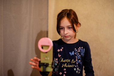 Mutlu genç bir kadın beyaz arka planda selfie çekiyor. Kız monopod ya da selfie çubuğuyla kendi videosunu çekiyor. Blogcu. Vlog. Kız internet ya da internet ağları için video çekiyor. Portre