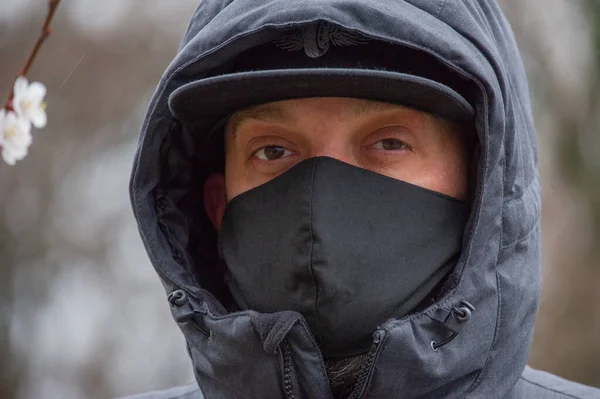 A man wearing a black respiratory mask on his face. A man in the street in a black mask. Virus. Coronavirus. A guy in the spring on the street in a respiratory mask to protect against infection virus