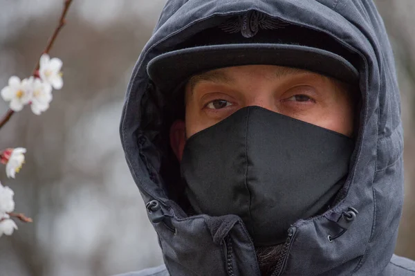 A man wearing a black respiratory mask on his face. A man in the street in a black mask. Virus. Coronavirus. A guy in the spring on the street in a respiratory mask to protect against infection virus