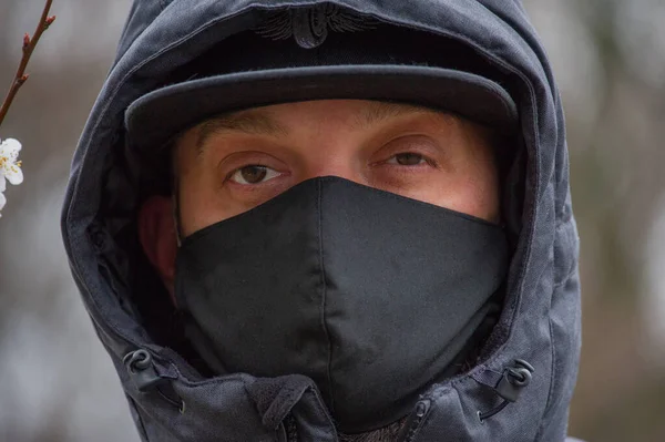 A man wearing a black respiratory mask on his face. A man in the street in a black mask. Virus. Coronavirus. A guy in the spring on the street in a respiratory mask to protect against infection virus