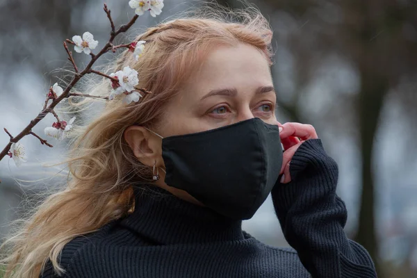 Beautiful young woman in spring clothes on the street with a medical face mask on. Closeup of a 30-year-old female in a respirator to protect against infection with coronavirus - Covid19. Coronavirus