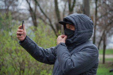 Yüzüne siyah solunum maskesi takan bir adam. Coronavirus. Enfeksiyon virüsünden korunmak için sokakta solunum maskesi takan bir adam. Bir adam kendini akıllı telefondan fotoğraflıyor..