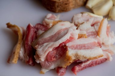 Sarımsaklı pastırma. Çavdar ekmekli sarımsak. Beyaz tahtada dilimlenmiş pastırma, sarımsak ve ekmek..