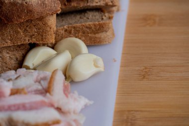 Sarımsaklı pastırma. Çavdar ekmekli sarımsak. Beyaz tahtada dilimlenmiş pastırma, sarımsak ve ekmek..