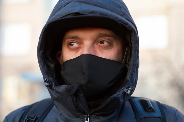 A man wearing a black respiratory mask on his face. A man in the street in a black mask. Virus. Coronavirus. A guy in the spring on the street in a respiratory mask to protect against infection virus