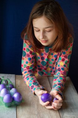 Mutlu Paskalyalar. Kız ve mor renkli yumurtalar. Paskalya gelenekleri. Ergen, kız 9 yaşında. Şarlatan bir kız. Puantiyeli elbise giymiş bir çocuk. Tatiller, ilkbahar