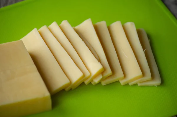 Sliced cheese on cutting board. Top view. Sliced hard cheese on a green board. Cheese