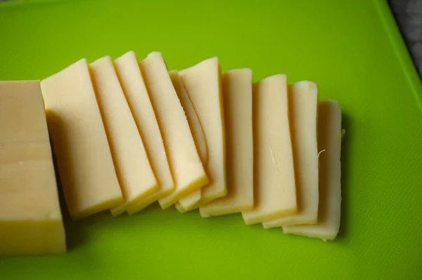 Sliced cheese on cutting board. Top view. Sliced hard cheese on a green board. Cheese