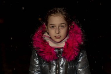 Dokuz yaşında güzel bir kızın portresi. 9 yaşında mavi ceketli bir kız. Kışın okul çocuğu. Ergen. Kış ve kar. Karlı bir akşam. Çocuk karın tadını çıkarıyor. Eko kürklü ceket.