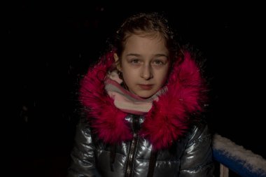 Dokuz yaşında güzel bir kızın portresi. 9 yaşında mavi ceketli bir kız. Kışın okul çocuğu. Ergen. Kış ve kar. Karlı bir akşam. Çocuk karın tadını çıkarıyor. Eko kürklü ceket.