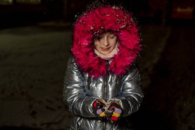 Dokuz yaşında güzel bir kızın portresi. 9 yaşında mavi ceketli bir kız. Kışın okul çocuğu. Ergen. Kış ve kar. Karlı bir akşam. Çocuk karın tadını çıkarıyor. Eko kürklü ceket.