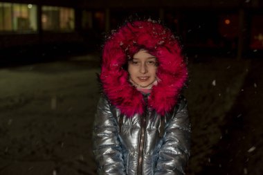 Dokuz yaşında güzel bir kızın portresi. 9 yaşında mavi ceketli bir kız. Kışın okul çocuğu. Ergen. Kış ve kar. Karlı bir akşam. Çocuk karın tadını çıkarıyor. Eko kürklü ceket.