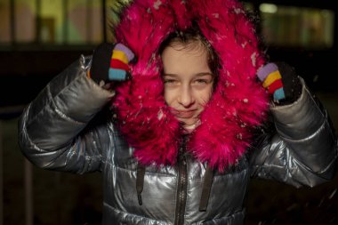 Dokuz yaşında güzel bir kızın portresi. 9 yaşında mavi ceketli bir kız. Kışın okul çocuğu. Ergen. Kış ve kar. Karlı bir akşam. Çocuk karın tadını çıkarıyor. Eko kürklü ceket.