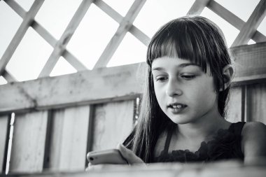 Küçük kız telefona bakıyor. 8-9 yaşındaki bir kız telefona bakıyor. Tatlı mutlu çocuk portresi cep telefonu ve yerli teknoloji konseptiyle internet oyunu oynayarak eğleniyor.