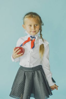 Altı yaşında beyaz tişörtlü bir kız mavi stüdyo arka planında izole edilmiş, güzel Avrupalı görünümlü çocuk kapalı alanda kameraya gülümsüyor, Z jenerasyonu konseptine. Mavi arka planda kız öğrenci