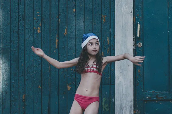 Bir çocuk Noel Baba şapkasıyla oynuyor. Noel Baba şapkalı mutlu küçük kız. Yazın açık havada. Yeni yıl ya da Noel serisi fotoğrafları.