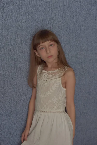女孩9岁背景蓝色墙纸 这个孩子在病毒传播期间一直呆在家里 女学生在家里 穿着白花边衣服的学龄小女孩 Z代儿童 — 图库照片