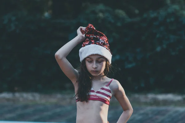 子供はサンタの帽子で遊んでいます 夏に屋外でサンタクロースの帽子の幸せな女の子 コンセプト新年や写真のクリスマスシリーズ プールでサンタクロースの帽子の小さな女の子 — ストック写真