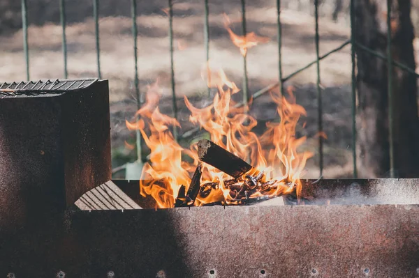 Portable metal grill with burning wood and red fire. Barbecue on the street. Fire and charcoal grilled. Barbecue equipment. BBQ picnic. Bonfire safety at the cottage concept. Bonfire grill