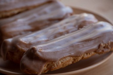 Kremalı kremalı kremalı kek. Üzerine kahverengi ve beyaz şekerli krema dökülmüş muhallebi kekleri. Çay ya da kahve için tatlı ikramları. Yakın plan. Seçici odaklanma. Kremalı pasta. Tatlı. Bej bir tabakta dört kek